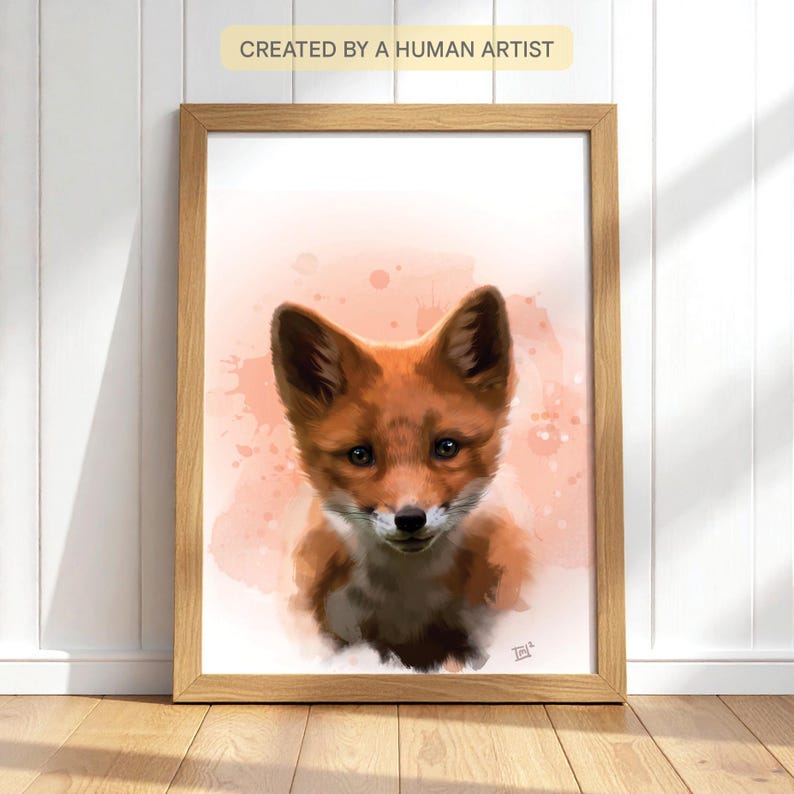Puede incluir: Una impresi&oacute;n en acuarela enmarcada de un cachorro de zorro. El zorro tiene pelaje naranja y blanco, con orejas grandes y ojos oscuros. El fondo es rosa suave con salpicaduras de pintura. El texto "CREATED BY A HUMAN ARTIST" est&aacute; en la parte superior.