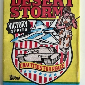 May include: A yellow Topps Desert Storm trading card pack featuring the text Victory Series and Coalition for Peace. The graphic includes a fighter jet, a tank, and a soldier in camouflage. The bottom indicates 8 trading cards and 1 sticker.