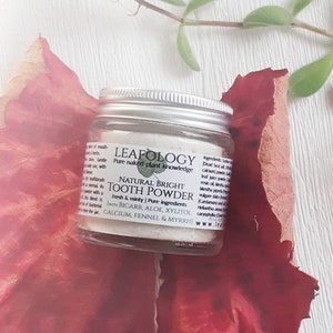 May include: A small white jar of natural bright tooth powder with a green leaf logo and the text "LEAFOLOGY Pure naked plant knowledge" and "NATURAL BRIGHT TOOTH POWDER Fresh & minty | Pure ingredients (with BICARB, ALOE, XYLITOL, CALCIUM, FENNEL & MYRRH)"
