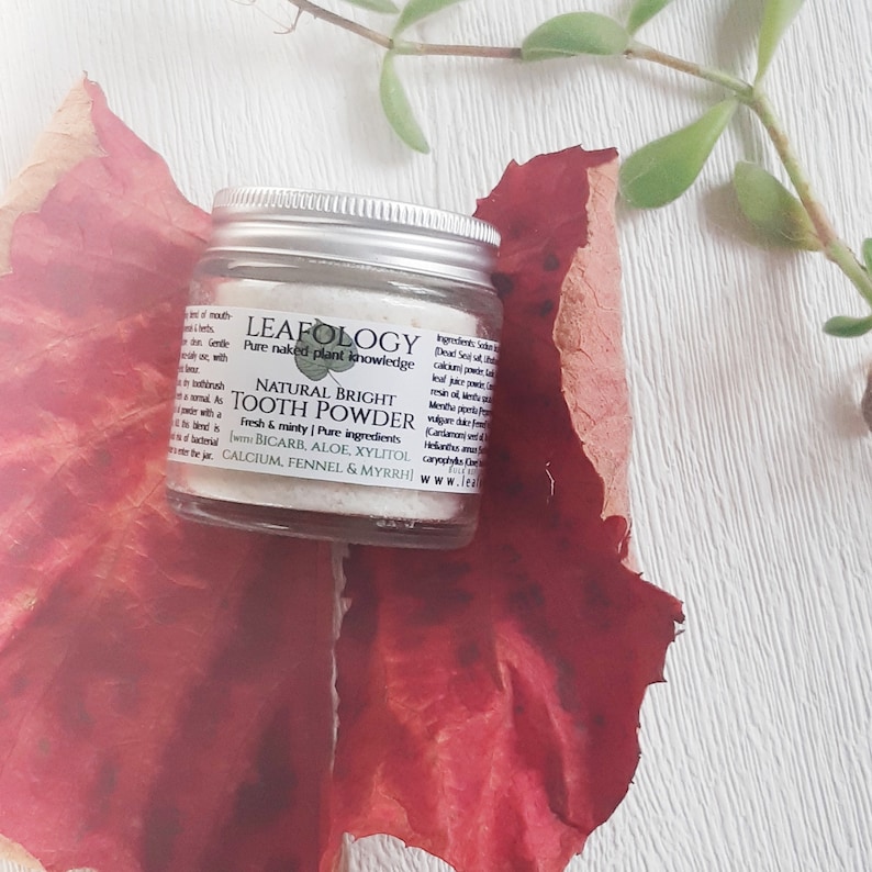 Puede incluir: Un peque&ntilde;o tarro blanco de polvo de dientes natural brillante con un logotipo de hoja verde y el texto "LEAFOLOGY Pure naked plant knowledge" y "NATURAL BRIGHT TOOTH POWDER Fresh & minty | Pure ingredients (with BICARB, ALOE, XYLITOL, CALCIUM, FENNEL & MYRRH)"