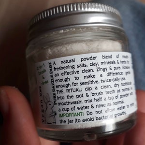 Puede incluir: Un frasco de vidrio con una etiqueta blanca que dice "Pure Dazzle Dust" y contiene un polvo blanco. La etiqueta tambi&eacute;n incluye instrucciones para usar el polvo como cepillo y enjuague 2 en 1, y como enjuague bucal. La etiqueta tambi&eacute;n indica que el producto es vegano y contiene 60 ml.