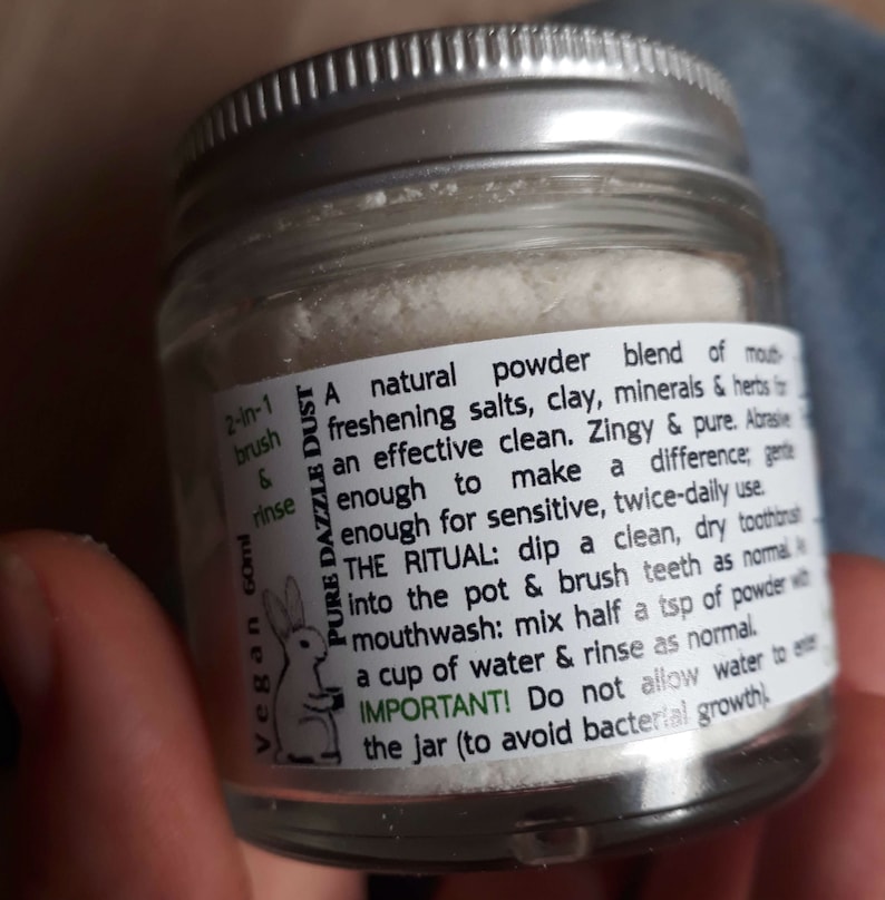 Puede incluir: Un frasco de vidrio con una etiqueta blanca que dice "Pure Dazzle Dust" y contiene un polvo blanco. La etiqueta tambi&eacute;n incluye instrucciones para usar el polvo como cepillo y enjuague 2 en 1, y como enjuague bucal. La etiqueta tambi&eacute;n indica que el producto es vegano y contiene 60 ml.