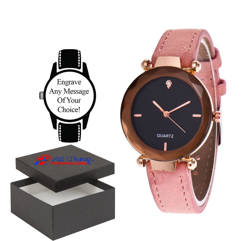 May include: A pink leather band watch with a black face and gold accents. The watch has a small diamond on the face and says "QUARTZ" below the hands. The watch comes in a black box with the text "All Things Personalized" on the top.