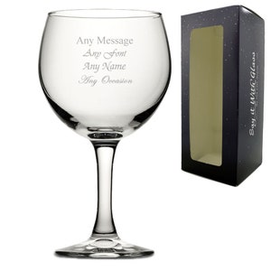 May include: A clear, stemmed wine glass with the text "Any Message, Any Font, Any Name, Any Occasion" etched on the bowl. The glass is next to a black box with a window and the text "Say it With Glass".