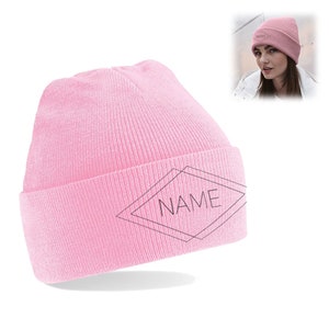 Può includere: Un berretto rosa chiaro con risvolto. Il berretto presenta un design geometrico con la parola "NAME" all'interno. Un'immagine più piccola mostra una persona che indossa lo stesso berretto.