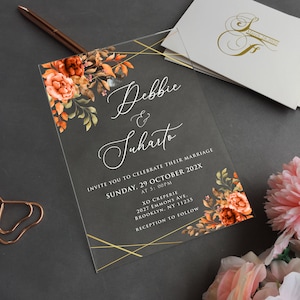 Może przedstawiać: Przezroczyste akrylowe zaproszenie ślubne z złotymi akcentami i kwiatowym wzorem z pomarańczowymi i brązowymi kwiatami. Zaproszenie zawiera tekst "Debbie & Suharto, Invite you to celebrate their marriage, Sunday, 29 October 202X, at 5:00PM, XO Creperie, 2027 Emmons Ave, Brooklyn, NY 11235, Reception to follow."