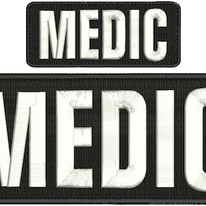 以下が含まれることがあります： 白文字で「MEDIC」と書かれた黒と白の刺繍パッチ2枚