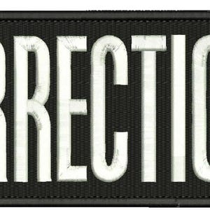 May include: A rectangular black embroidered patch with a stitched border. The word CORRECTIONS is displayed in large, bold, white capital letters across the center. The lettering features a textured, slightly distressed appearance with white thread.
