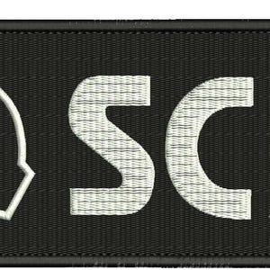 May include: Black and white embroidered patch with the logo of the SCP Foundation. The logo is a circle with a downward pointing arrow and two outward pointing arrows. The text "SCP" is written in white letters.