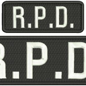 Könnte beinhalten: Zwei gestickte Aufnäher mit den Buchstaben "R.P.D." in Weiß auf schwarzem Hintergrund. Der größere Aufnäher ist rechteckig, der kleinere darüber. Die Aufnäher sind wahrscheinlich für Kleidung oder Accessoires.