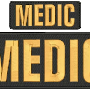 May include: Two embroidered patches with the word "MEDIC". The text is in a gold color, and the patches have a black background with a stitched border. One patch is smaller than the other.