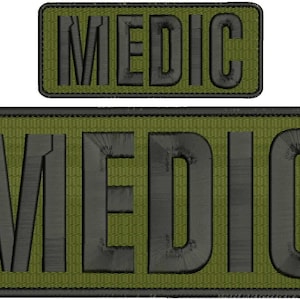 May include: Two embroidered patches with the word "MEDIC". The patches have a green background with black lettering. The larger patch is rectangular, and the smaller patch is also rectangular.