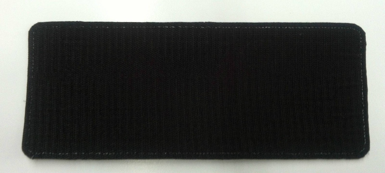 May include: A black rectangular patch of fabric with a stitched border. The patch is made of a soft, textured material.