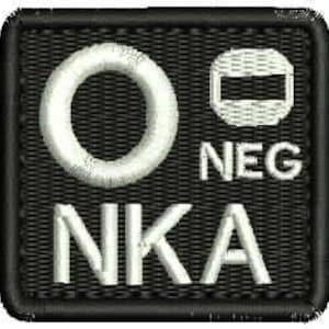 以下が含まれることがあります： 白の刺繍が施された黒いパッチ。パッチには円形、長方形、そして「NKA」と「NEG」の文字が刺繍されています。