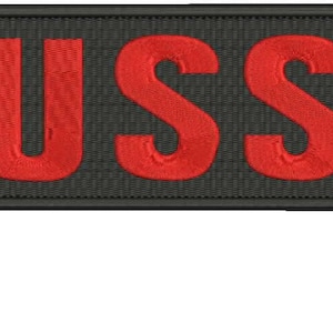 May include: Embroidered patch featuring the letters "USS" in red. The letters are stitched onto a dark grey rectangular patch with a black border. This patch is likely designed for attachment to clothing or bags.