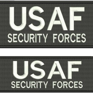 Könnte beinhalten: Zwei schwarze rechteckige Patches mit weiß gesticktem Text. Der obere Patch lautet "USAF SECURITY FORCES". Der untere Patch lautet "USAF SECURITY FORCES".