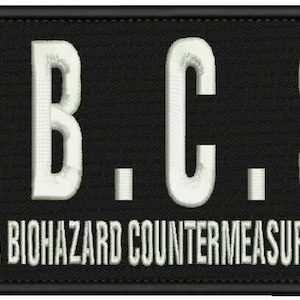 Könnte beinhalten: Schwarz-weißer gestickter Aufnäher mit dem Text "U.B.C.S." und den Worten "Umbrella Biohazard Countermeasure Service" darunter.