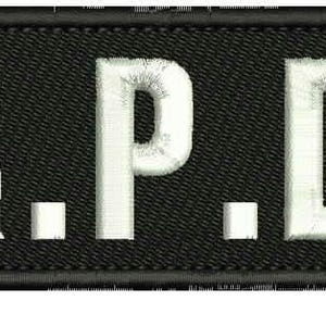 Könnte beinhalten: Schwarzer rechteckiger Patch mit weißen gestickten Buchstaben, die "R.P.D." lesen