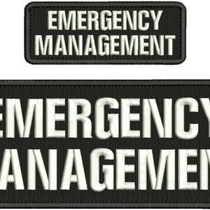May include: Two black embroidered patches with the text "EMERGENCY MANAGEMENT" in white. The larger patch is rectangular, and the smaller patch is above it. The patches are likely for uniforms or gear.