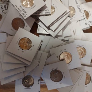 May include: A close-up view of a stack of white coin holders with US quarters inside. The coins are from different years and states, including California and Tennessee. The holders are labeled with the year and state of the coin.