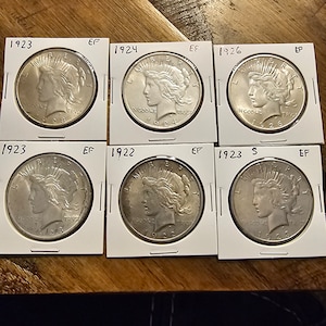 May include: Six silver Peace Dollar coins from 1922, 1923, 1924, 1926, and two from 1923, all in excellent condition.