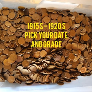 May include: A bin overflowing with copper-colored pennies. The text "1915S - 1920S PICK YOUR DATE AND GRADE" is superimposed in yellow. The coins are stacked, suggesting a collection of vintage or collectible pennies.