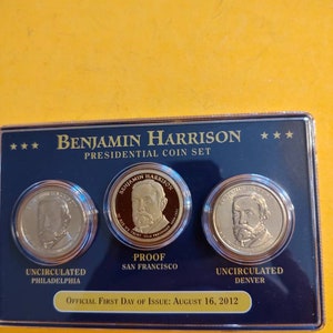May include: A set of three gold-colored coins featuring the portrait of Benjamin Harrison, the 23rd President of the United States. The coins are labeled "Uncirculated Philadelphia", "Proof San Francisco", and "Uncirculated Denver". The set is displayed in a blue and gold case with the text "Benjamin Harrison Presidential Coin Set" and "Official First Day of Issue: August 16, 2012".