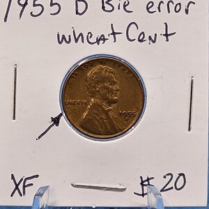 May include: A 1955 D Bie error wheat Cent coin, displayed on a white card. The coin is copper-colored with the text "IN GOD WE TRUST" and "LIBERTY" visible. The card has handwritten text: "1955 D Bie error wheat Cent" and "XF".