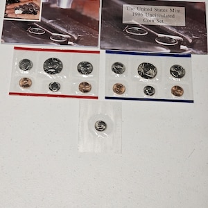 May include: A 1996 United States Mint Uncirculated Coin Set featuring two rectangular plastic holders with red and blue borders, each containing six coins, plus a single small coin in a separate square plastic pouch and an informational card.