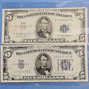 May include: Two vintage five-dollar bills. Each bill features a portrait of Abraham Lincoln and the text "FIVE DOLLARS" in a decorative font. The bills are printed in black and green ink on a cream-colored paper.