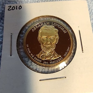 May include: A gold-colored coin with a portrait of Abraham Lincoln and the text "ABRAHAM LINCOLN 16th PRESIDENT 1861-1865" around the edge. The coin also has the text "IN GOD WE TRUST" and the year "2010" on it.