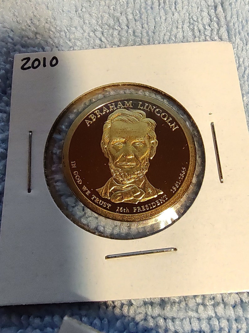 May include: A gold-colored coin with a portrait of Abraham Lincoln and the text "ABRAHAM LINCOLN 16th PRESIDENT 1861-1865" around the edge. The coin also has the text "IN GOD WE TRUST" and the year "2010" on it.