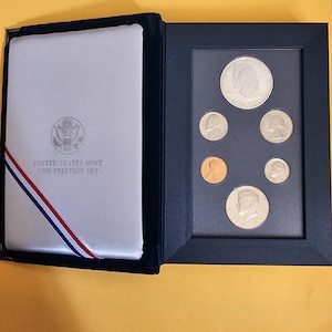 May include: A 1990 United States Mint Prestige Set, featuring a collection of coins. The set includes a variety of coins, displayed in a black frame. The set's cover is white with the text "UNITED STATES MINT 1990 PRESTIGE SET".