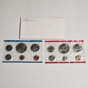 May include: A 1976 U.S. Mint uncirculated coin set featuring two plastic-sealed packets of coins. One packet has a blue border and the other a red border. Each packet contains a variety of silver-toned coins and one copper-toned penny.