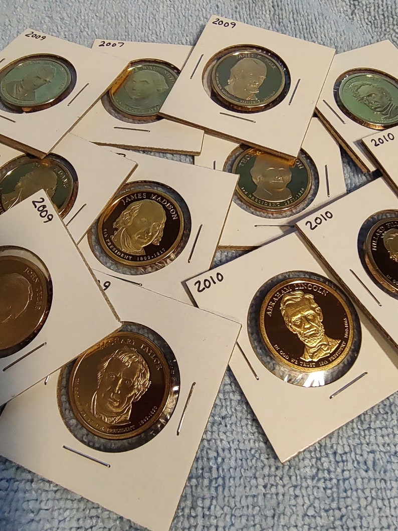 May include: A collection of gold-colored coins featuring portraits of U.S. presidents. The coins are displayed in white card holders with the year and president's name printed on them. The coins are part of the Presidential Dollar Coin Program.