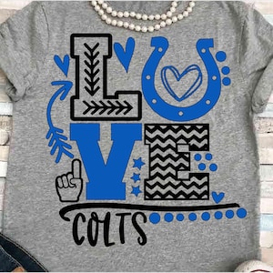 May include: A gray t-shirt with the word "LOVE" in blue and black letters. The "L" is decorated with an arrow and a leaf, the "O" is a horseshoe with a heart inside, the "V" is a blue letter with a star and a pointing finger, and the "E" is a black and white chevron pattern. The word "COLTS" is written in black below the word "LOVE".
