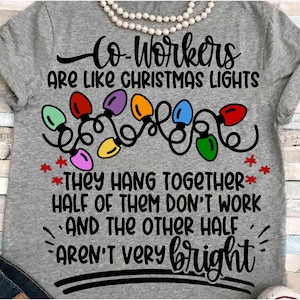 May include: A gray t-shirt with the text "Co-Workers are like Christmas Lights" and a string of colorful Christmas lights. The text continues with "They hang together, half of them don't work and the other half aren't very bright."