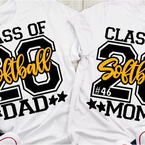 Puede incluir: Dos camisetas blancas con texto negro y amarillo. Las camisetas dicen "CLASS OF 23 Softball" con "#46" y "DAD" o "MOM" debajo. Cada camiseta tiene dos estrellas negras.