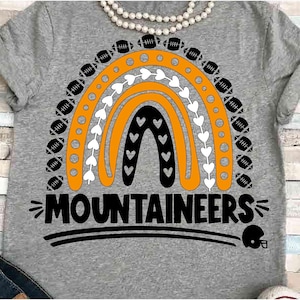 May include: Gray t-shirt with a black and orange rainbow design featuring footballs and hearts. The text "MOUNTAINEERS" is below the rainbow.