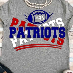 May include: Gray t-shirt with the word "PATRIOTS" in blue and white block letters. A blue football with the number 46 is above the word. Red and white accents complete the design.