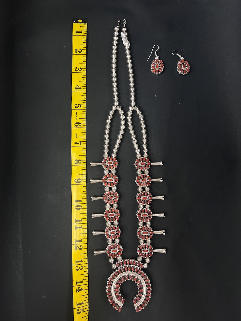 May include: A silver necklace with a horseshoe pendant and red coral beads. The necklace is 15 inches long and has a matching pair of earrings.