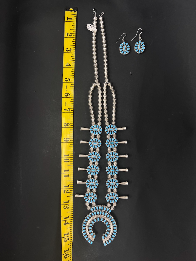 May include: A turquoise and silver Native American necklace with a horseshoe pendant and matching earrings. The necklace is approximately 15 inches long.