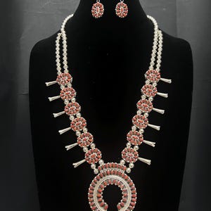 May include: A silver necklace with a horseshoe pendant and multiple round charms, all decorated with red coral stones. Matching earrings with red coral stones are also included.