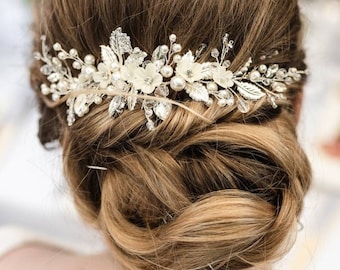 May include: A hair comb featuring a silver-toned wire base adorned with white floral accents, small round pearls, and clear crystals. The decorative piece is arranged in a horizontal, branch-like design with metallic leaves and delicate sprigs.