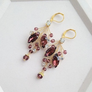 Op de afbeelding: Een paar oorhangers met een gouden draadontwerp en paarse en heldere kristallen.