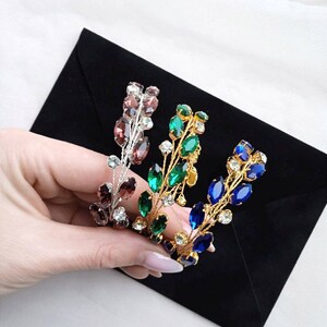 May include: Three gold hair combs with different coloured crystal accents. The combs are decorated with small, clear crystals and larger, oval-shaped crystals in shades of purple, green, and blue.