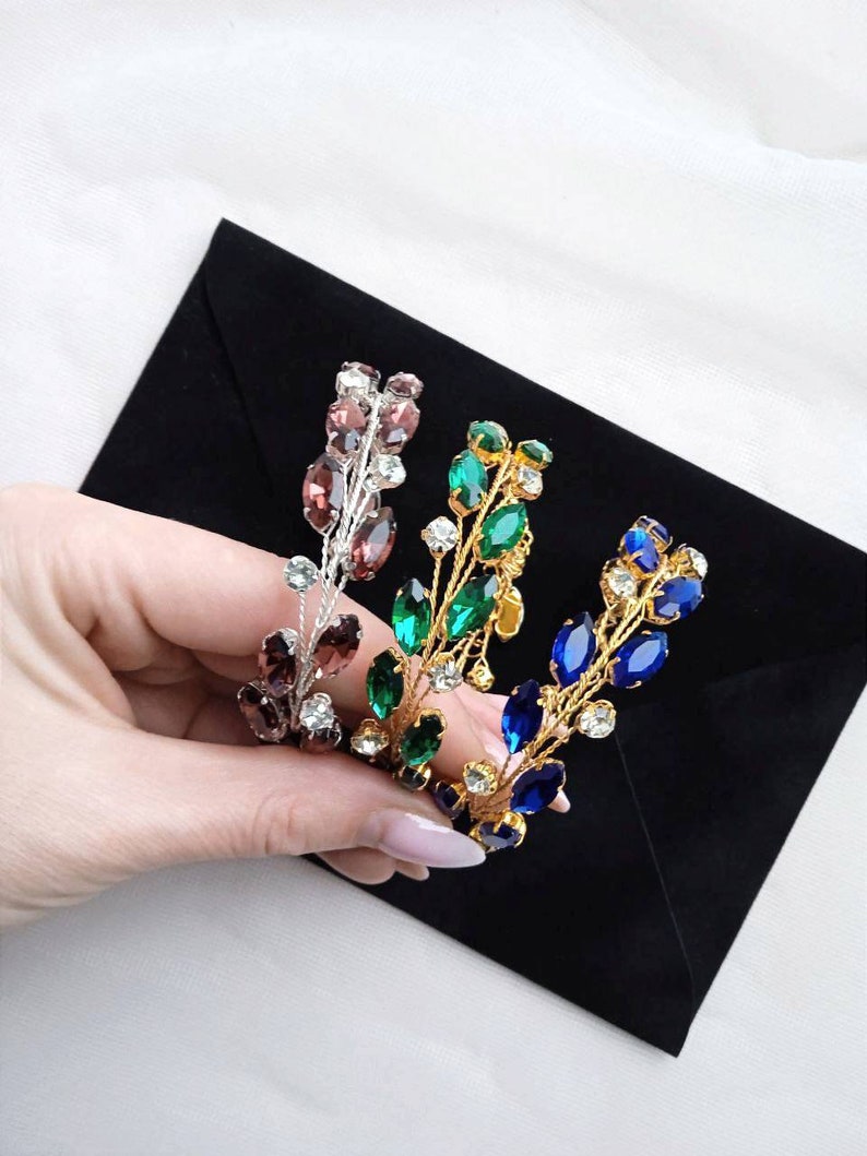 May include: Three gold hair combs with different coloured crystal accents. The combs are decorated with small, clear crystals and larger, oval-shaped crystals in shades of purple, green, and blue.