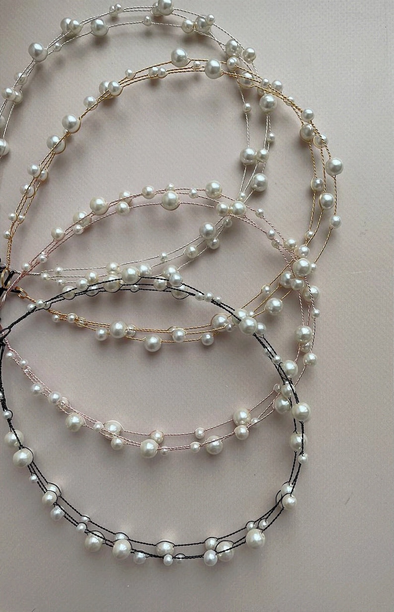 May include: Four strands of pearl jewelry with different colored wires. The strands are made of small white pearls and thin wires in gold, silver, pink, and black.