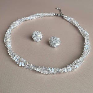 Può includere: Un set di collana e orecchini a bottone abbinati in cristallo trasparente. La collana è a girocollo e gli orecchini sono rotondi. I gioielli brillano con una moltitudine di sfaccettature, riflettendo la luce.