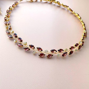 May include: A delicate gold necklace with a double row of marquise-shaped purple rhinestones and small clear rhinestones. The necklace is designed to resemble a vine with leaves.